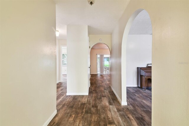 hallway featuring baseboards, dark wood finished floors, and arched walkways