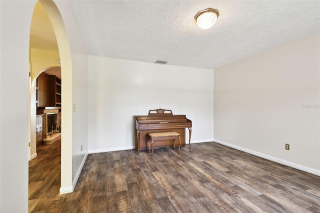 unfurnished room with arched walkways, dark wood-style flooring, a textured ceiling, and baseboards