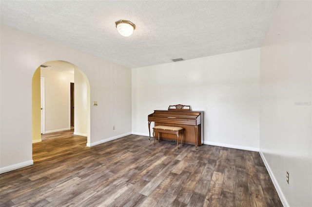 empty room featuring arched walkways, dark wood-style flooring, visible vents, and baseboards