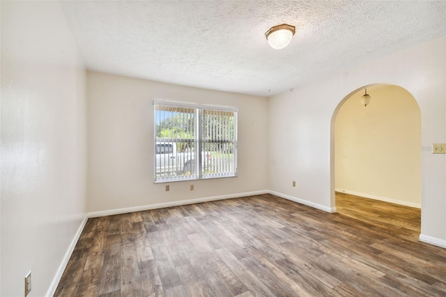 empty room with arched walkways, dark wood-style flooring, a textured ceiling, and baseboards