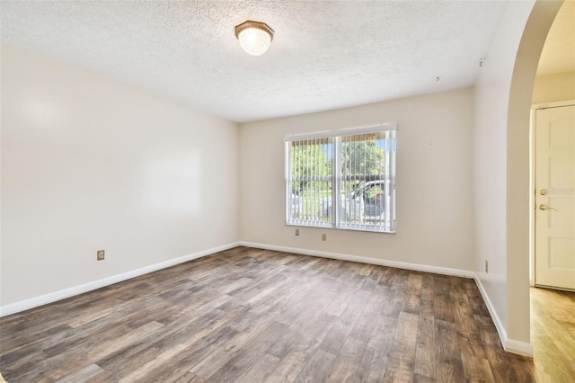 unfurnished room featuring baseboards, arched walkways, and dark wood finished floors