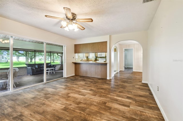 interior space featuring baseboards, arched walkways, ceiling fan, dark wood-type flooring, and a textured ceiling