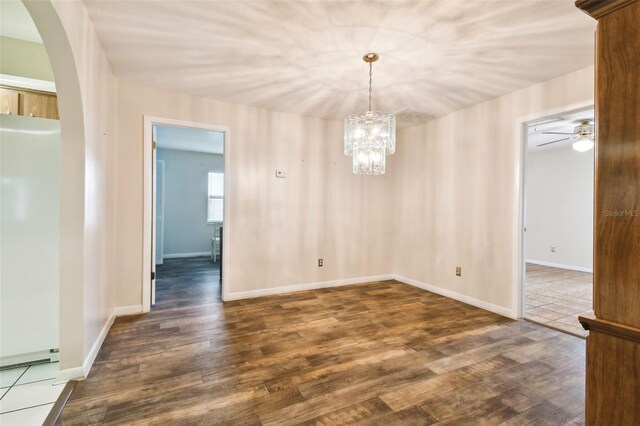 unfurnished room with baseboards, arched walkways, dark wood-style flooring, and ceiling fan with notable chandelier