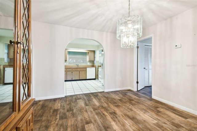 unfurnished dining area with arched walkways, baseboards, a notable chandelier, and light wood finished floors