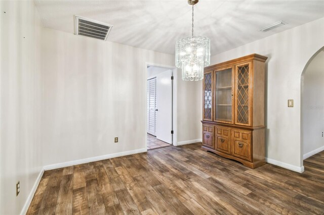 unfurnished dining area with dark wood-type flooring, arched walkways, visible vents, and baseboards