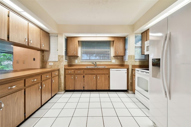 kitchen featuring light tile patterned floors, light countertops, brown cabinetry, a sink, and white appliances