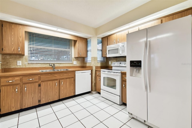 kitchen with light countertops, decorative backsplash, brown cabinetry, a sink, and white appliances