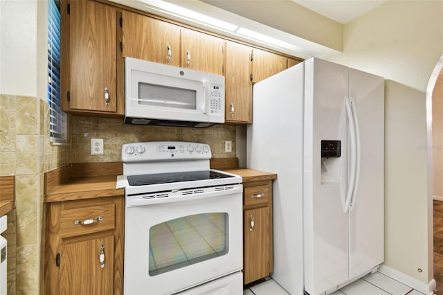 kitchen with brown cabinetry, white appliances, light countertops, and backsplash