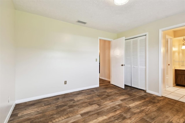 unfurnished bedroom with a textured ceiling, a closet, visible vents, and dark wood-type flooring