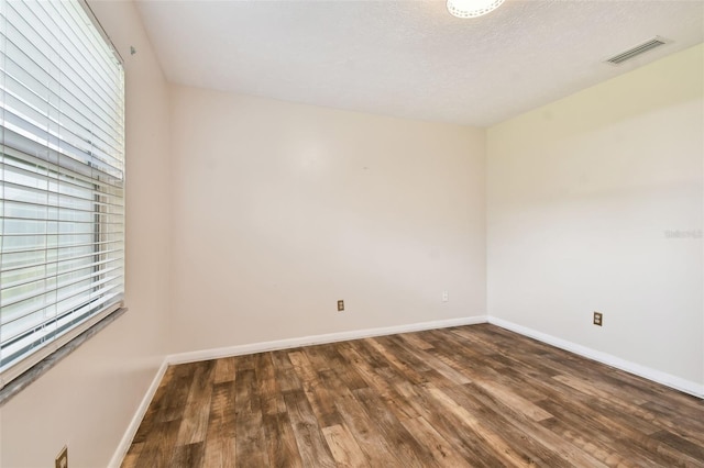 empty room featuring visible vents, a textured ceiling, baseboards, and wood finished floors