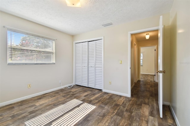 unfurnished bedroom with a closet, visible vents, dark wood-type flooring, a textured ceiling, and baseboards