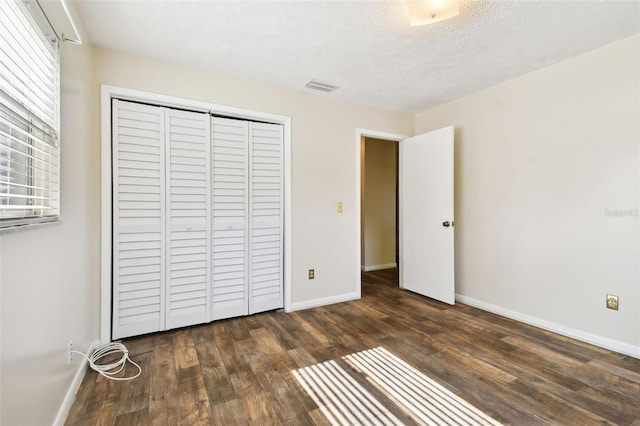 unfurnished bedroom featuring a textured ceiling, dark wood-style flooring, visible vents, baseboards, and a closet