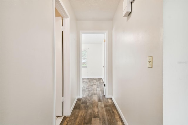 hall with dark wood-type flooring, a textured ceiling, and baseboards