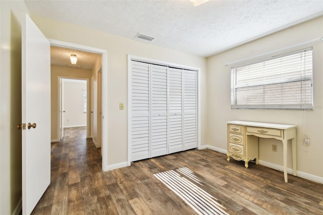 unfurnished bedroom with dark wood-style flooring, visible vents, a textured ceiling, and baseboards