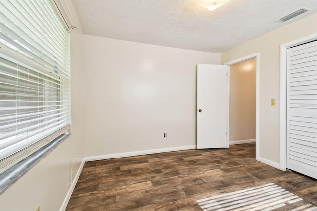 unfurnished bedroom featuring dark wood-style floors, visible vents, a textured ceiling, and baseboards