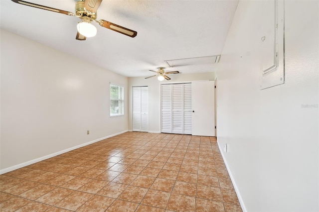 unfurnished bedroom featuring light tile patterned floors, ceiling fan, a textured ceiling, baseboards, and two closets