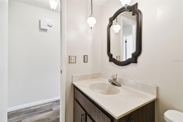 bathroom featuring toilet, baseboards, wood finished floors, and vanity