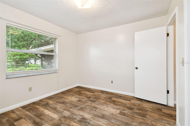 empty room featuring a textured ceiling, dark wood finished floors, and baseboards