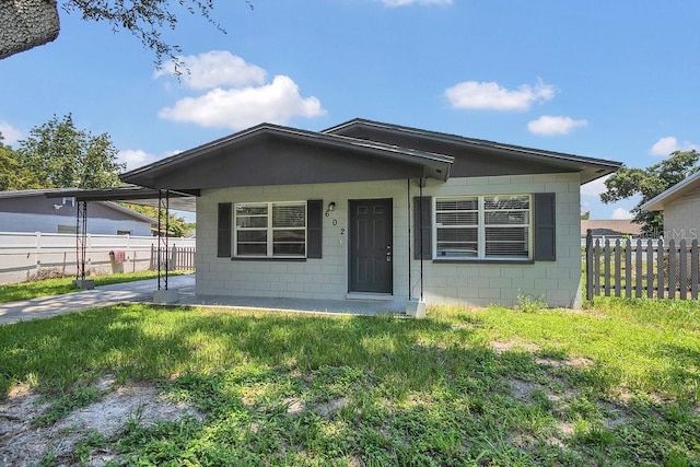 bungalow with concrete block siding, a front yard, fence, an attached carport, and driveway