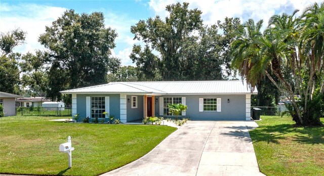 ranch-style home featuring stucco siding, metal roof, fence, driveway, and a front lawn