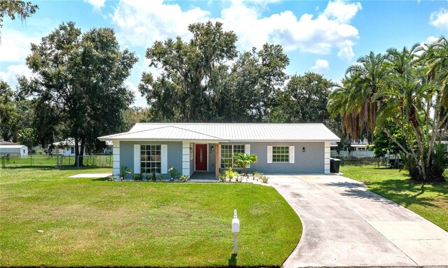 ranch-style home with concrete driveway, metal roof, fence, a front lawn, and stucco siding