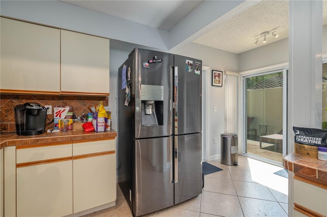 kitchen featuring a textured ceiling, backsplash, stainless steel fridge with ice dispenser, tile counters, and light tile patterned flooring