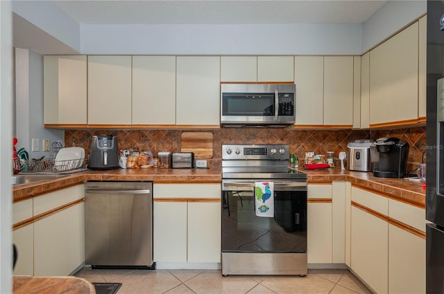 kitchen featuring light tile patterned floors, tasteful backsplash, stainless steel appliances, and cream cabinets