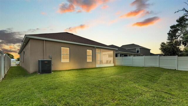 back house at dusk with a lawn and central air condition unit