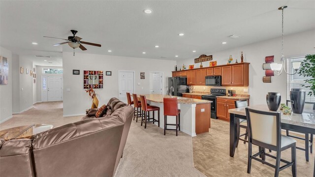 kitchen with a kitchen bar, ceiling fan, black appliances, a kitchen island, and light colored carpet