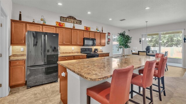 kitchen featuring a kitchen breakfast bar, decorative backsplash, a kitchen island with sink, black appliances, and sink