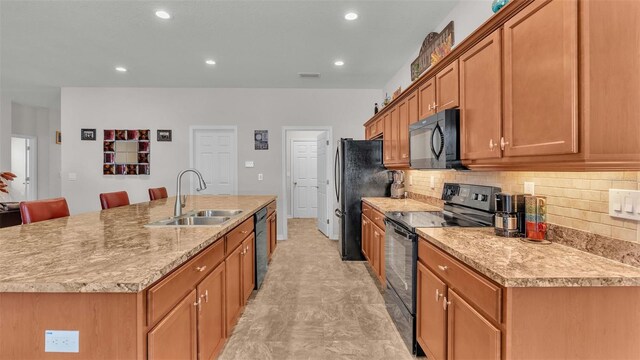 kitchen with black appliances, light tile patterned flooring, a center island with sink, tasteful backsplash, and sink