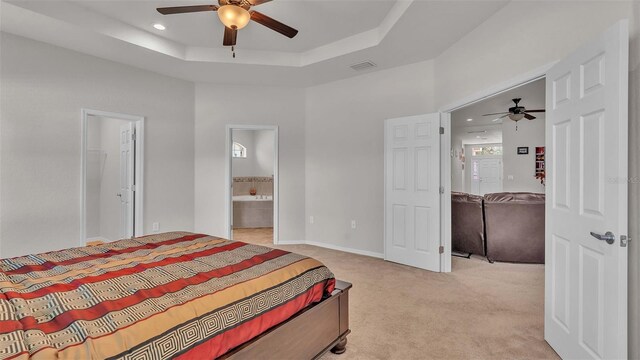 bedroom with ceiling fan, ensuite bathroom, light carpet, and a tray ceiling