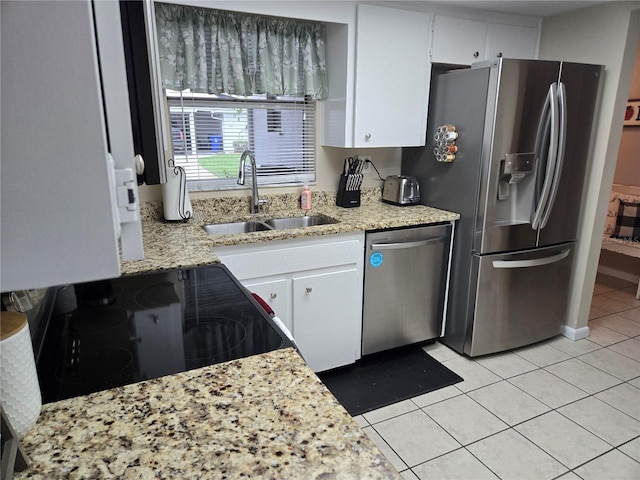 kitchen featuring light tile patterned floors, appliances with stainless steel finishes, white cabinets, a sink, and light stone countertops