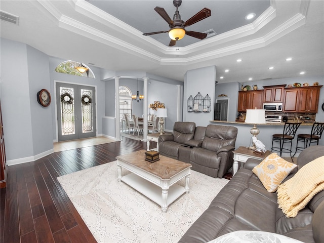 living room with a tray ceiling, dark wood-type flooring, ceiling fan with notable chandelier, and ornamental molding