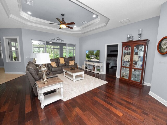 living room featuring dark hardwood / wood-style flooring, a tray ceiling, ceiling fan, and crown molding