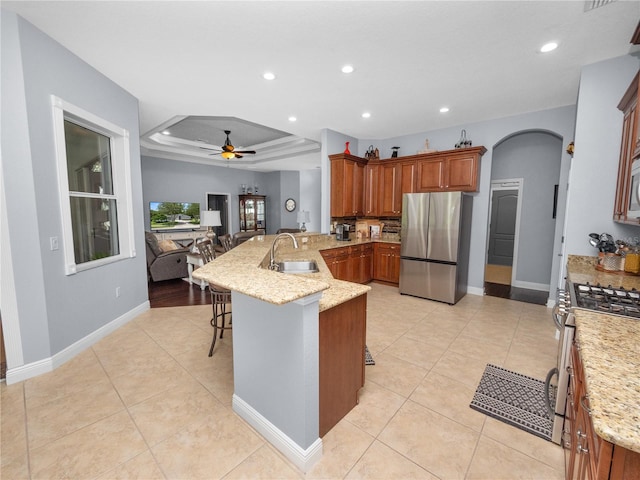 kitchen featuring ceiling fan, a tray ceiling, a kitchen bar, kitchen peninsula, and stainless steel appliances