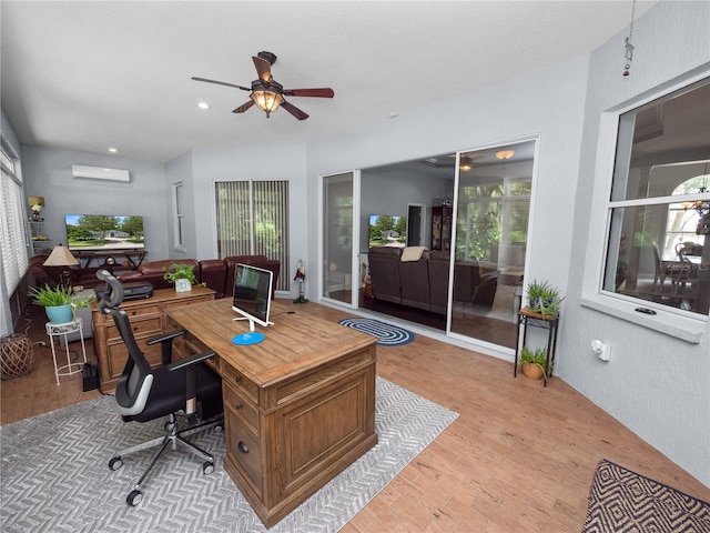 office featuring a wall mounted air conditioner, ceiling fan, and light hardwood / wood-style floors