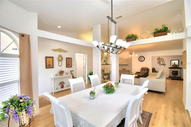 dining area featuring a textured ceiling, high vaulted ceiling, light hardwood / wood-style floors, and an inviting chandelier