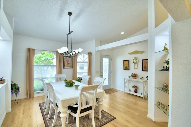 dining area featuring light wood-type flooring, vaulted ceiling, a notable chandelier, and a textured ceiling