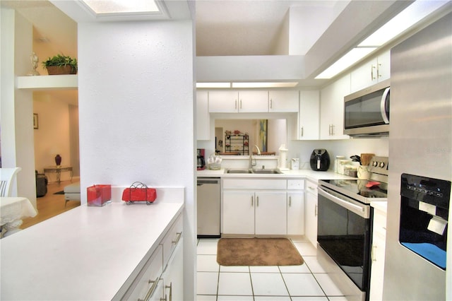 kitchen featuring appliances with stainless steel finishes, white cabinetry, light tile patterned floors, and sink