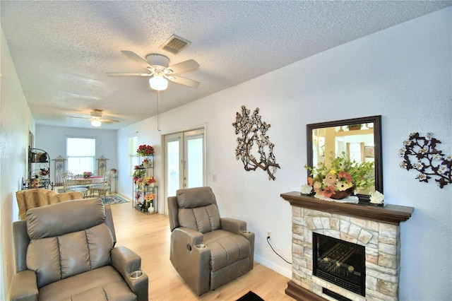 living room with a fireplace, light hardwood / wood-style flooring, ceiling fan, and a healthy amount of sunlight