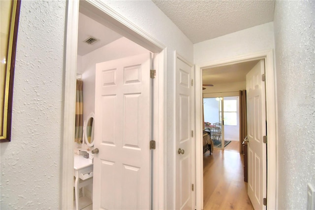 corridor with a textured ceiling and light hardwood / wood-style flooring