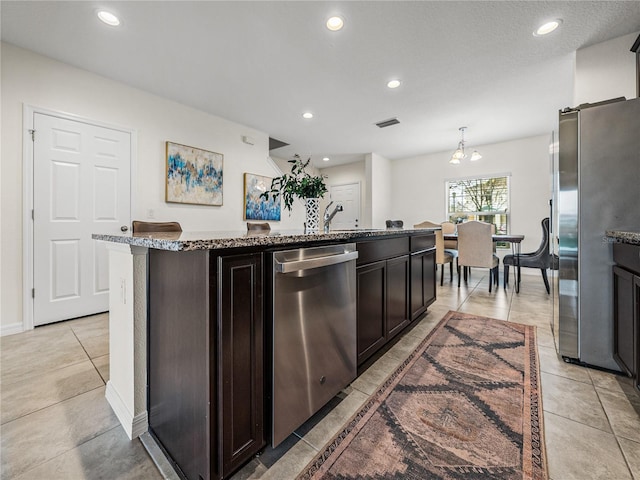 kitchen featuring stainless steel appliances, an inviting chandelier, an island with sink, dark brown cabinets, and pendant lighting