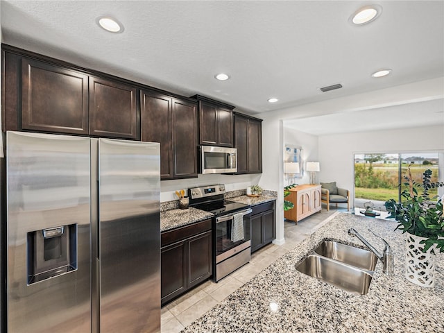 kitchen with stainless steel appliances, sink, light stone counters, light tile patterned flooring, and dark brown cabinets