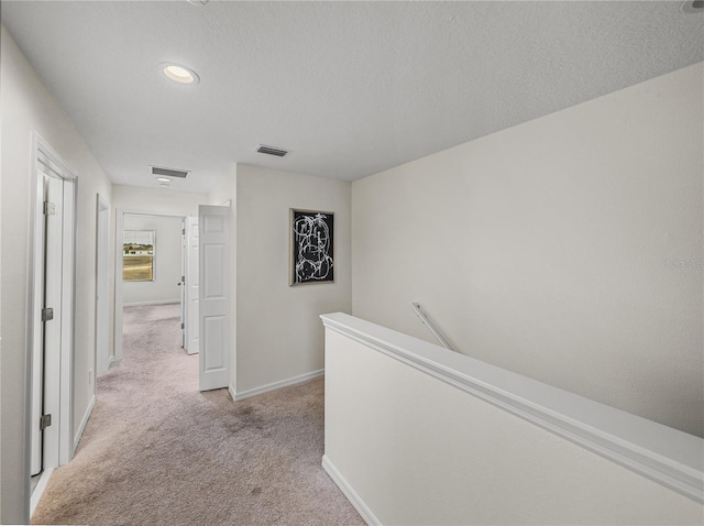 corridor with light colored carpet and a textured ceiling