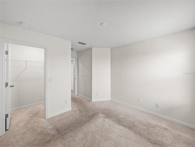 unfurnished bedroom with a walk in closet, a textured ceiling, a closet, and light carpet