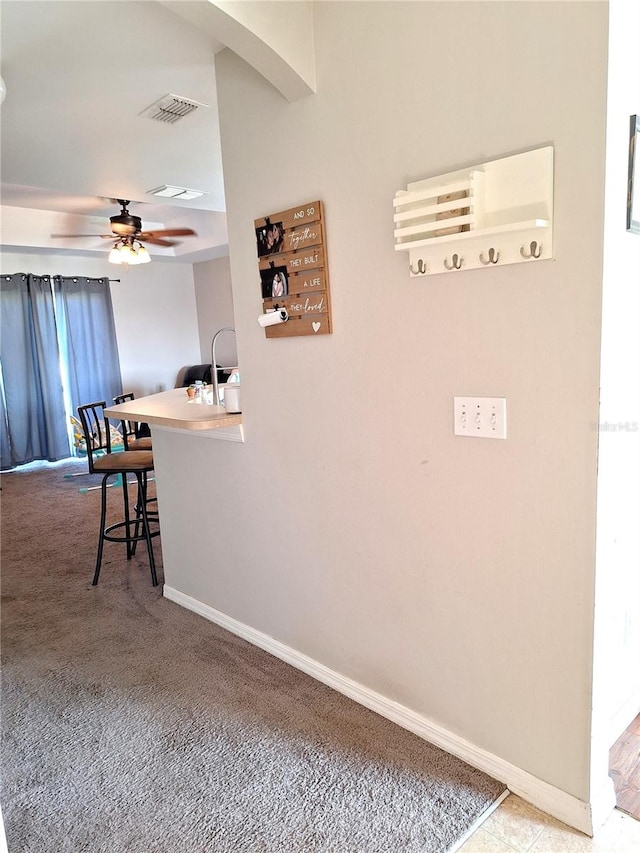 interior space featuring ceiling fan, a breakfast bar area, kitchen peninsula, and light carpet