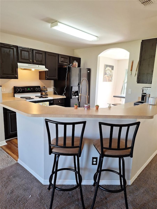 kitchen featuring a breakfast bar area, under cabinet range hood, range with electric stovetop, light countertops, and black fridge