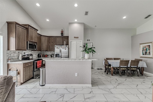 kitchen featuring appliances with stainless steel finishes, backsplash, dark brown cabinets, light tile patterned floors, and a center island