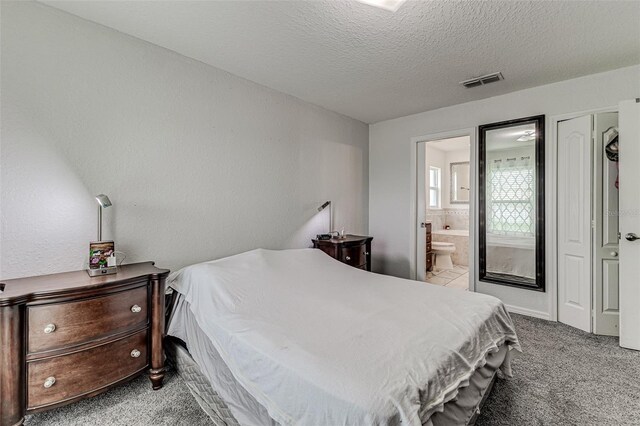 carpeted bedroom with ensuite bathroom and a textured ceiling